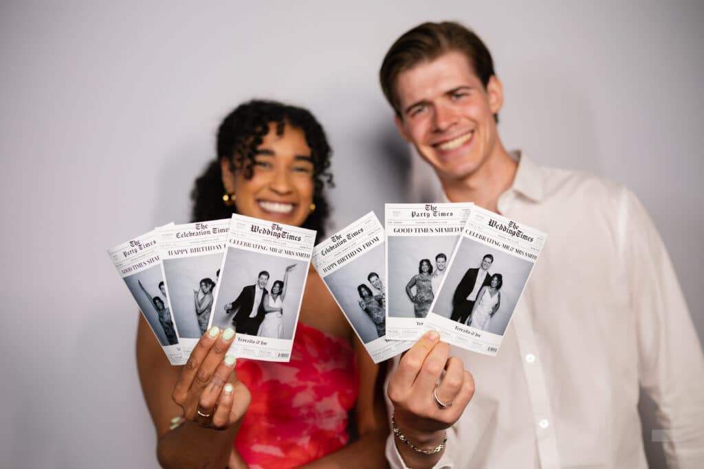 Man and woman holding news paper-style photo booth prints