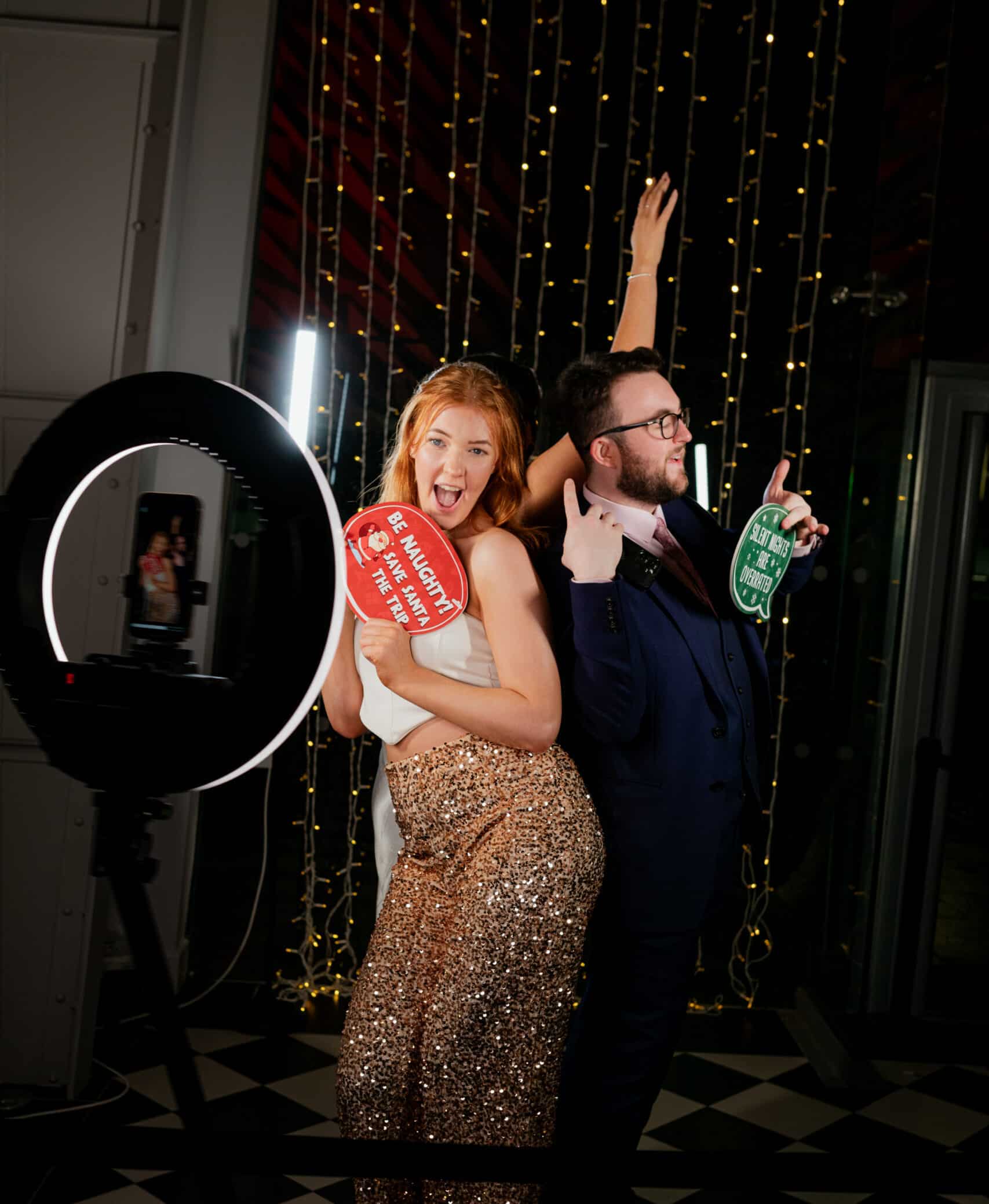 Guests at a party posing with playful signs in front of a photo booth, showcasing fun and memorable moments created by Glitz IQ's customized event services.