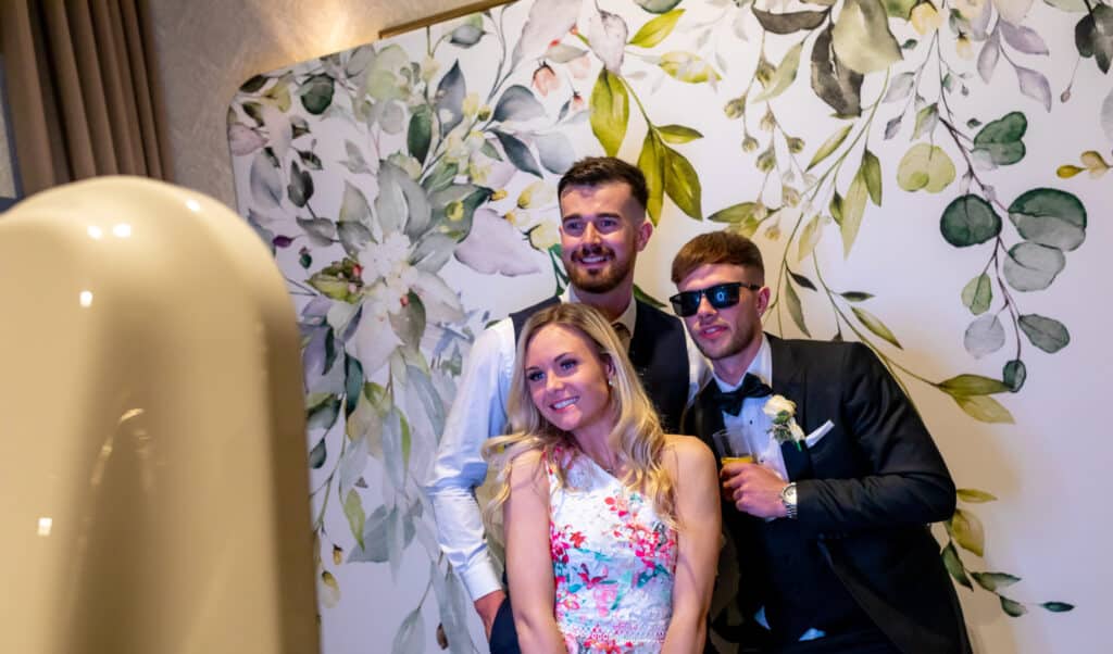 Group of three smiling individuals posing in front of a floral backdrop, enjoying a photo booth experience at a corporate event in Cleveland.
