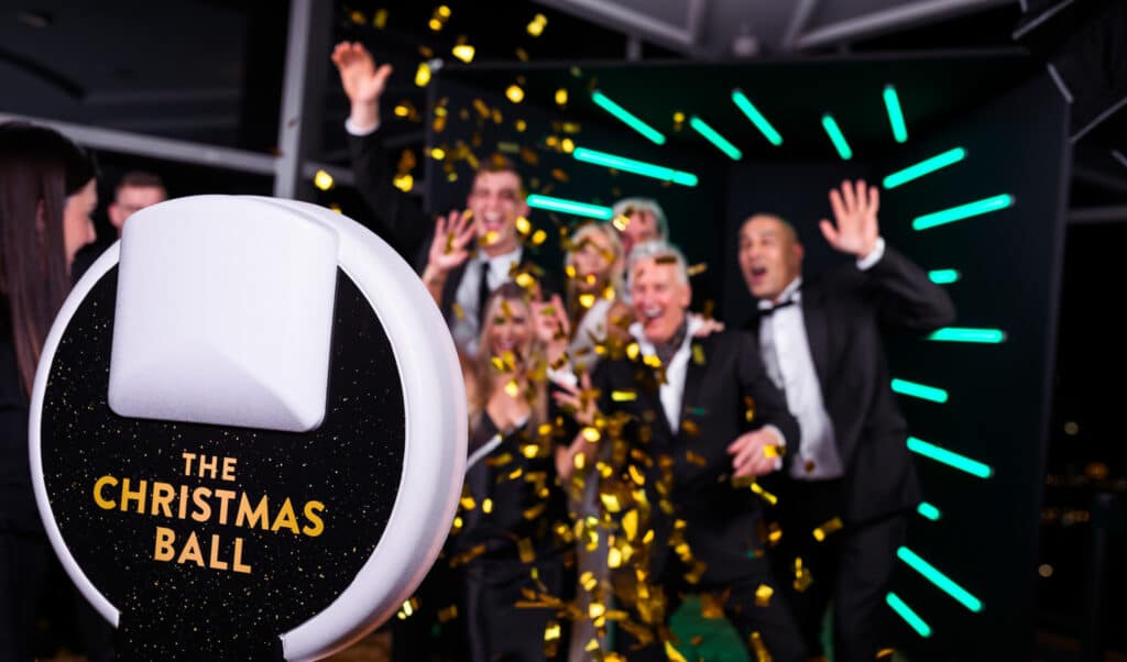 Photo booth at corporate event with guests celebrating, confetti falling, and a sign reading "The Christmas Ball," highlighting user-generated content and social sharing potential for Cleveland events.