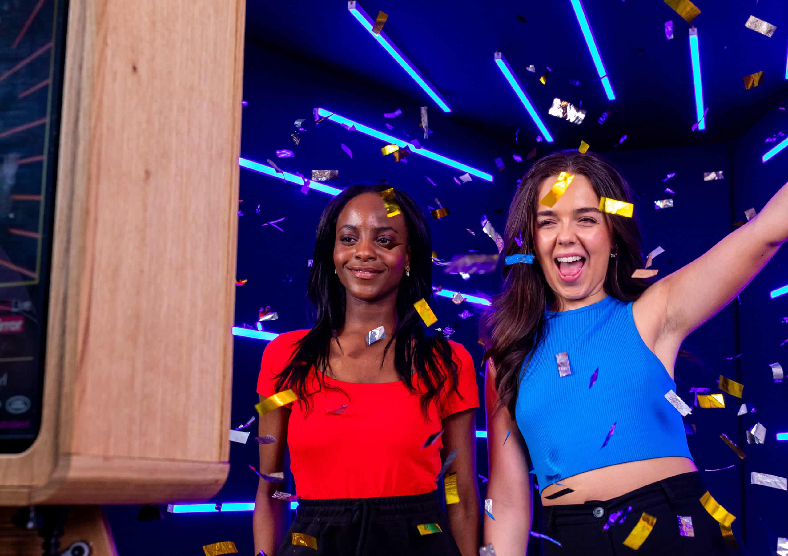 Two women posing for a photo with an open air photo booth in front of a neon backdrop