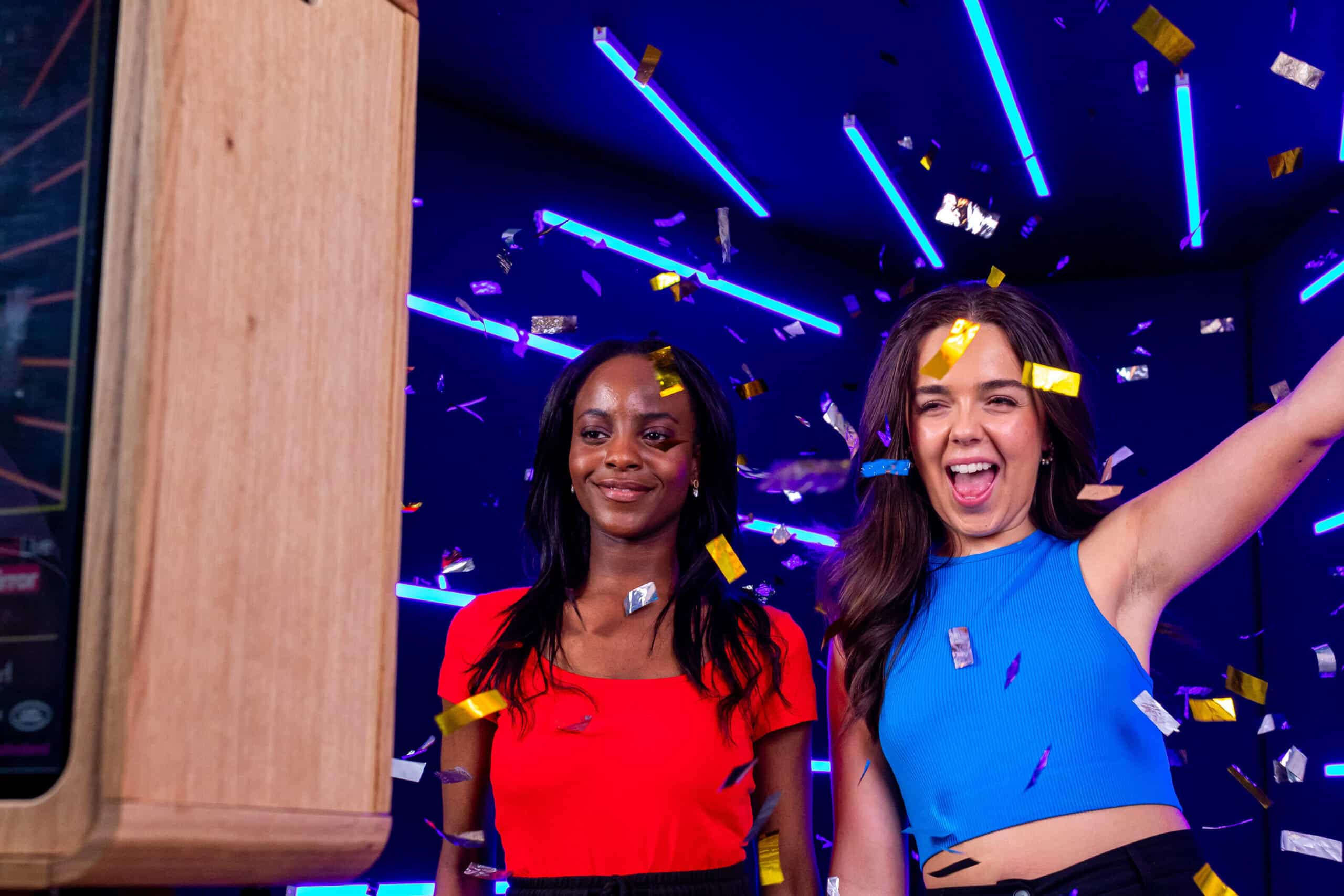 Two women posing for a photo with an open air photo booth in front of a neon backdrop